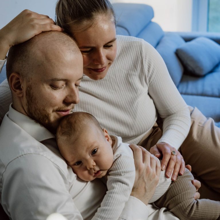 Eine Mutter und ein Vater halten ihr Baby auf dem Schoß, alle wirken liebevoll und entspannt.