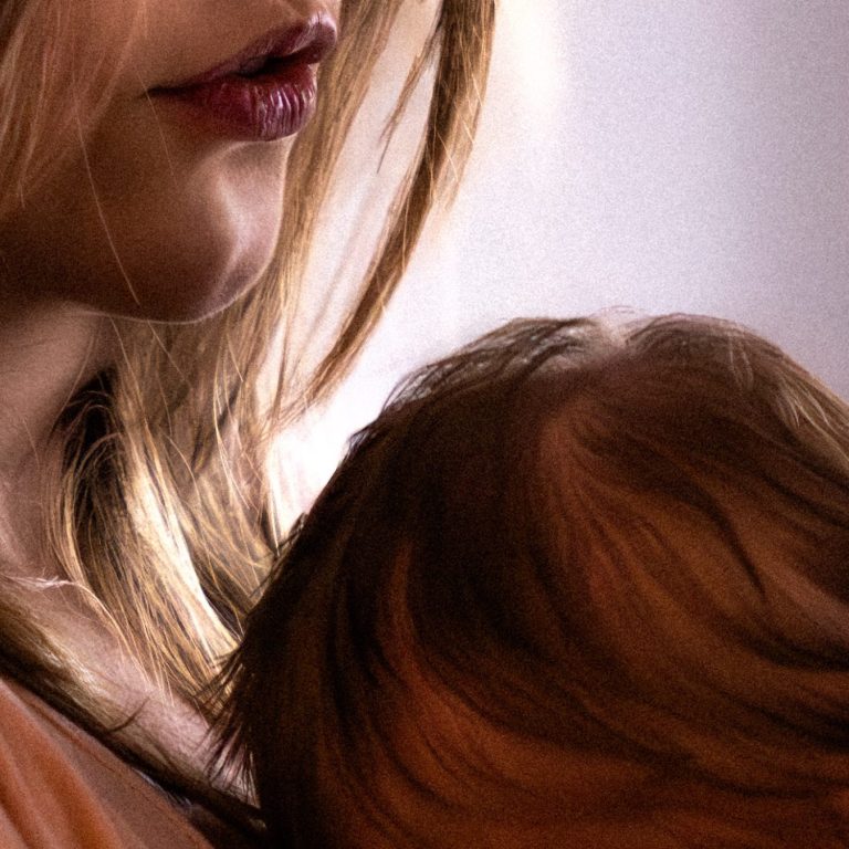 Newborn-Fotoshooting Eine Mutter und ein Vater halten ihr Baby auf dem Schoß, alle wirken liebevoll und entspannt.