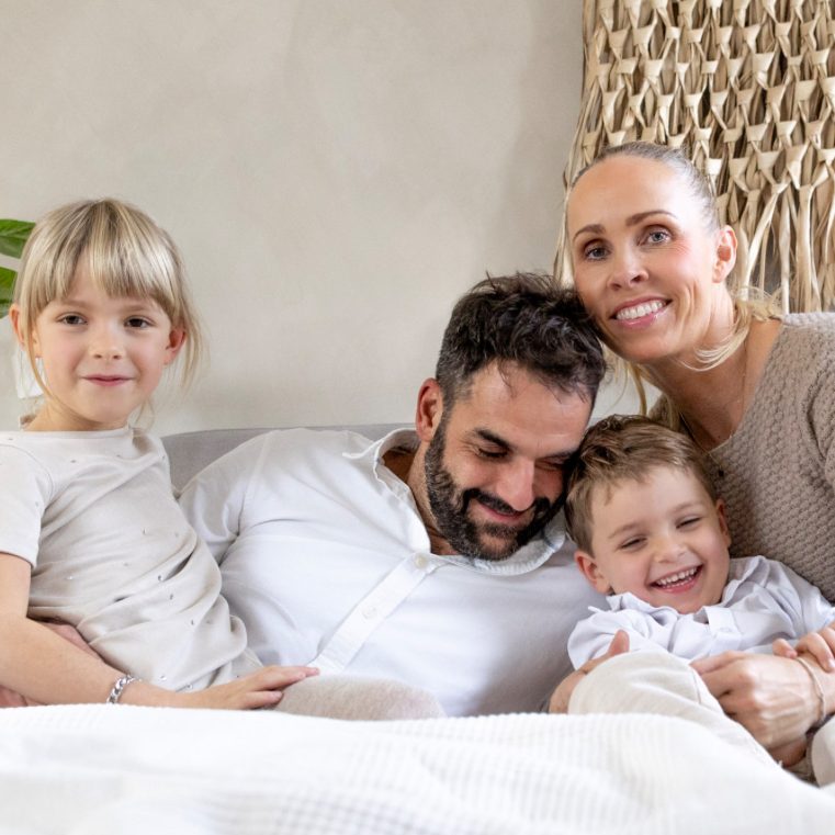 Eine Familie sitzt lächelnd auf einem Sofa, mit zwei kleinen Kindern und Erwachsenen.