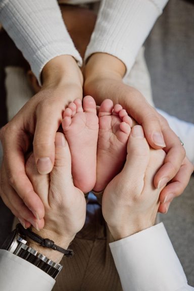 Hände umgeben kleine Füße, die auf einer weichen Oberfläche liegen.