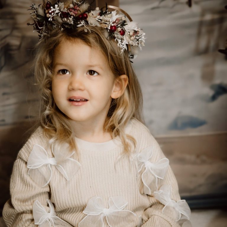 Ein Mädchen mit Blumenkranz und einem lächelnden Gesicht in einem Boho Hintergrund.