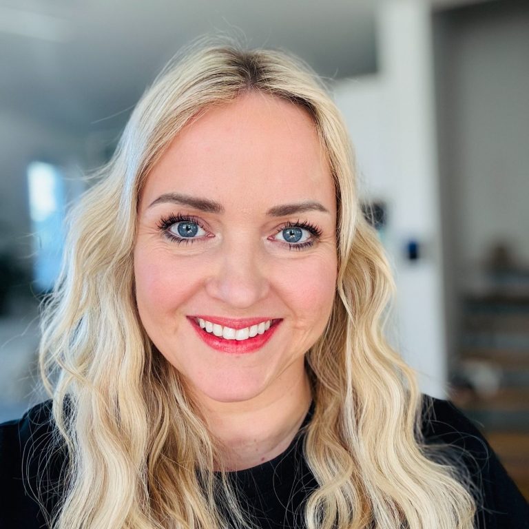 Porträt einer lächelnden Frau mit langen, welligen blonden Haaren und rotem Lippenstift. Fotografin familara Fotografie.